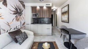 A modern living room with a sofa, a coffee table, and a dining area with a table and chairs. A kitchen with a microwave and a sink is visible in the background. - L'OISEAU PARADIS - Studio Gare de Vaise (Lyon)