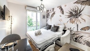 A modern bedroom with a bed, a desk, and a chair. There is a window with a view of greenery outside. - L'OISEAU PARADIS - Studio Gare de Vaise (Lyon)