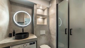 A modern bathroom with a round mirror, a black sink, a washing machine, a toilet, and a glass shower enclosure. - LA PALMERAIE - Studio Valmy Metro Station (Lyon)