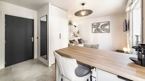 A modern dining area with a wooden table and chairs, a black door, and a wall-mounted light fixture. - LA PALMERAIE - Studio Valmy Metro Station (Lyon)