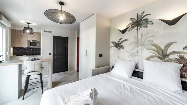 A modern hotel room with a bed, a desk, and a kitchenette. - LA PALMERAIE - Studio Valmy Metro Station (Lyon)