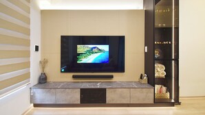 Ein modernes Wohnzimmer mit einem an der Wand befestigten Flachbildfernseher, einer eingebauten Unterhaltungseinheit und einer Glastheke mit Dekorationselementen.