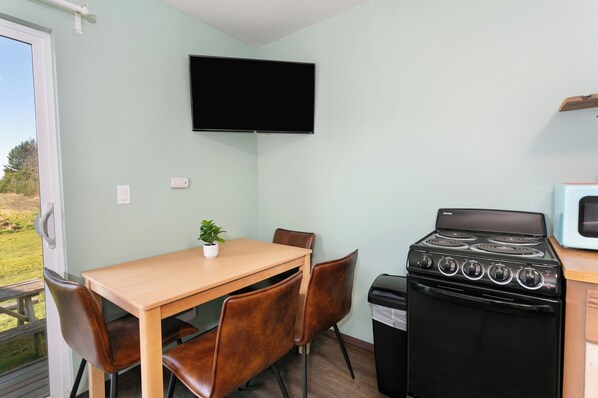 Una cocina compacta con una mesa de madera, cuatro sillas, una estufa negra, un microondas y un televisor en la pared.