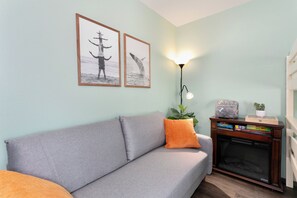 Una sala de estar con un sofá gris, cojines naranjas, cuadros enmarcados, una lámpara y una pequeña estantería.