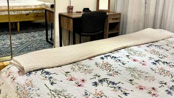 A hotel room with a bed, a desk, a chair, a mirror, and two shelves with plants.