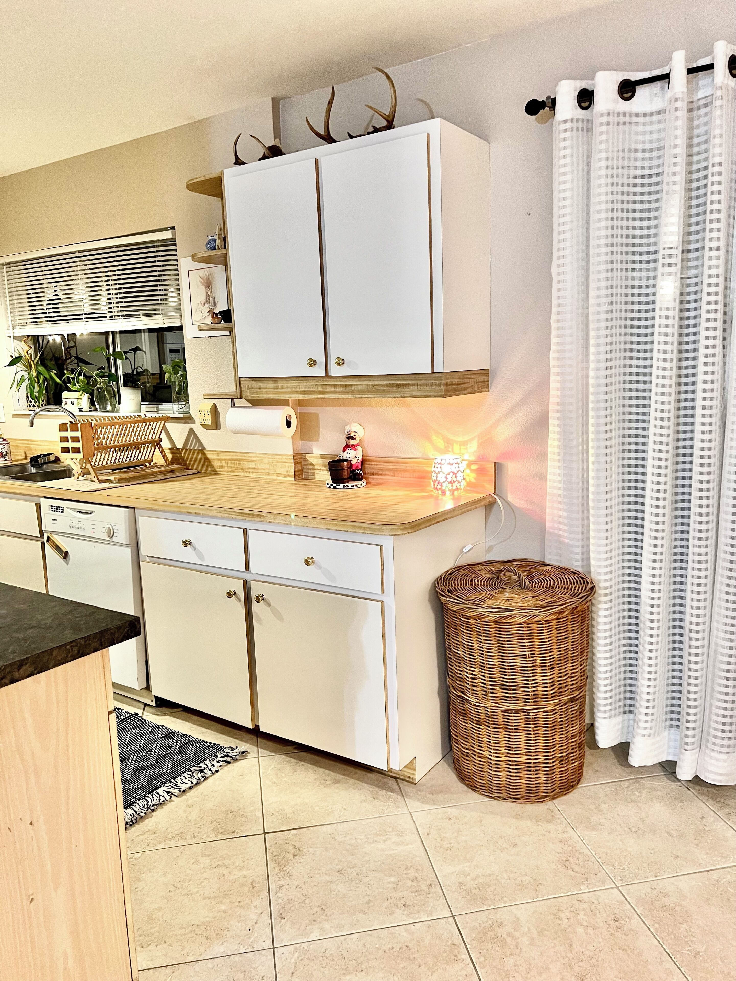Una cocina compacta con armarios blancos, encimera de madera y una cesta de mimbre.