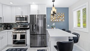 A modern kitchen with white cabinetry, stainless steel appliances, and a dining area with black chairs.