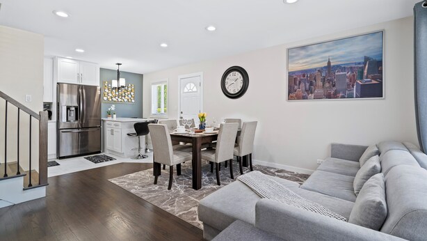 A modern kitchen with stainless steel appliances, a dining area with a wooden table and chairs, and a large cityscape painting on the wall.
