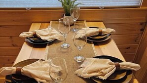 A wooden dining table with a woven placemat, set with plates, cutlery, and wine glasses. A small potted plant is on the table, and a book titled "The Walnut" is placed on the placemat. - Walnut Secluded Cabin at Lost Trails (Madison Township)