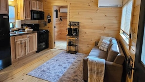 A cozy cabin interior with wooden walls, a kitchenette, a sofa, and a patterned rug. - Walnut Secluded Cabin at Lost Trails (Madison Township)