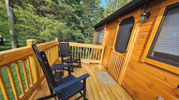 A wooden deck with two black rocking chairs and a small table, surrounded by a wooden railing. - Walnut Secluded Cabin at Lost Trails (Madison Township)