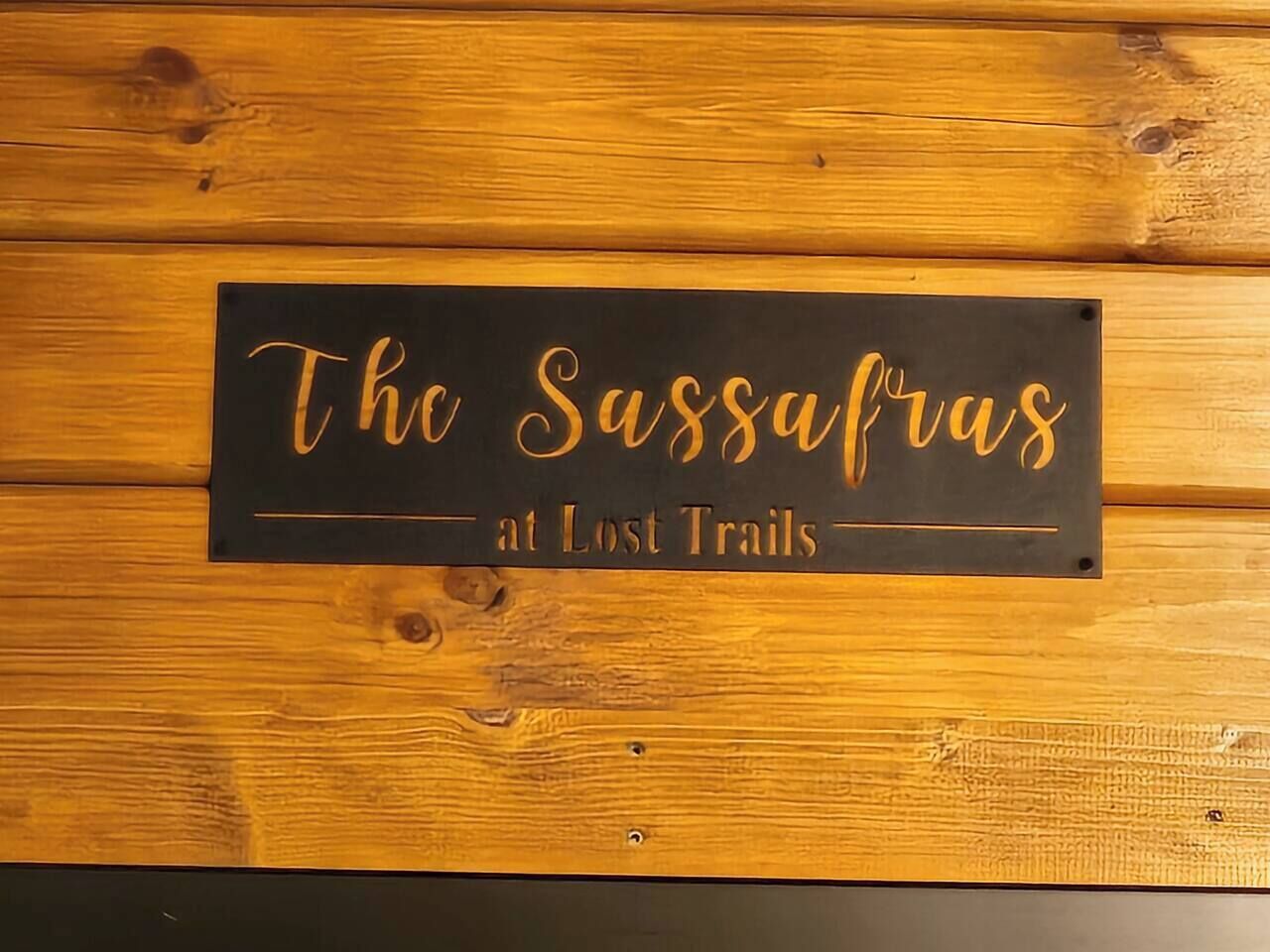 Et skilt med teksten "The Sassafras at Lost Trails" mod en træbaggrund.