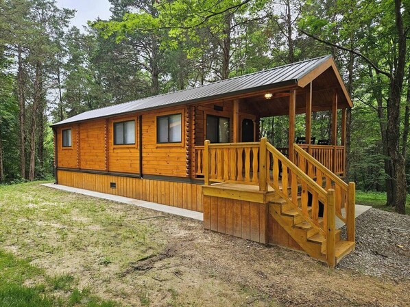 A log cabin with a wooden deck and staircase leading to a covered porch.