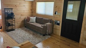 A cozy cabin interior with a wooden floor, a brown sofa, a coffee machine, and a door with a window.