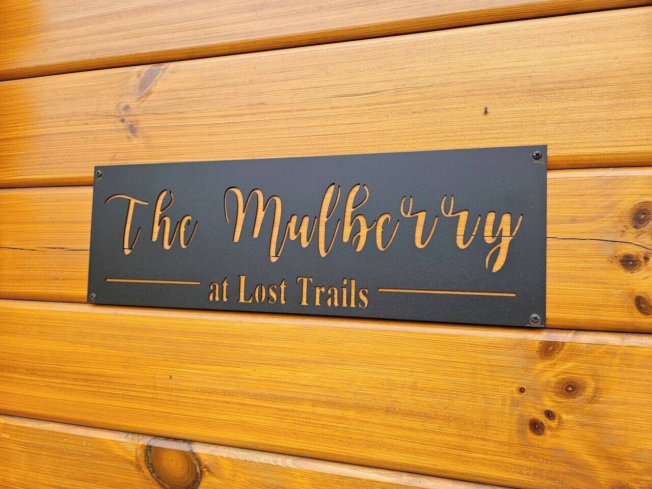Ein Schild mit dem Text "The Mulberry at Lost Trails" an einer Holzwand befestigt.