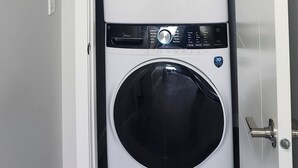 A front view of a double-door laundry room with two washing machines, one above the other, and a door handle on the right. - Charming 1-bedroom walkout pond backing suite with fitness machine, AC and bbq (Beaumont)
