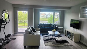 A modern living room with a sofa, coffee table, TV, and exercise equipment. - Charming 1-bedroom walkout pond backing suite with fitness machine, AC and bbq (Beaumont)
