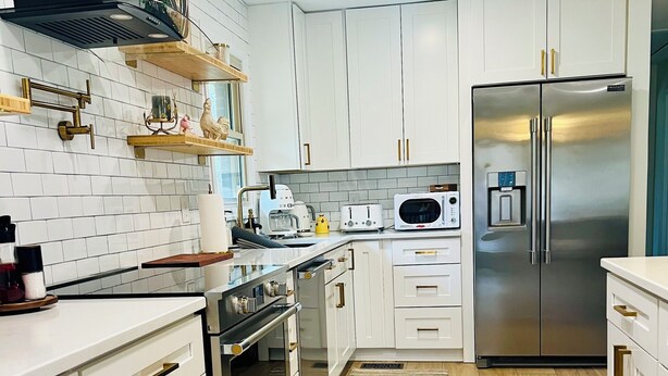 A modern kitchen with white cabinets, stainless steel appliances, and wooden flooring.