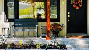 A building entrance with a bench, a large window, a door with a wreath, and a potted plant.