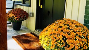 Une porte d’entrée décorée d’une guirlande, avec un pot de fleurs et des citrouilles sur le porche.