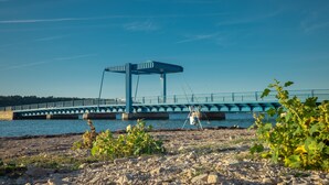 Un puente con una estructura azul cruzando un cuerpo de agua, con una orilla rocosa al frente.