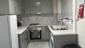 A compact kitchen with a refrigerator, oven, sink, and a washing machine.