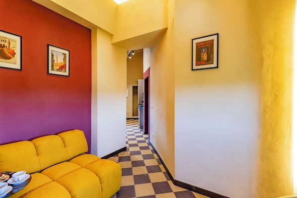 Un corridoio d'hotel con pavimento a scacchi, un divano giallo e quadri appesi alle pareti.