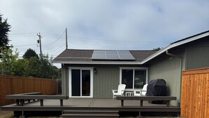Ein Garten mit überdachter Terrasse, Grill und Holzzaun.