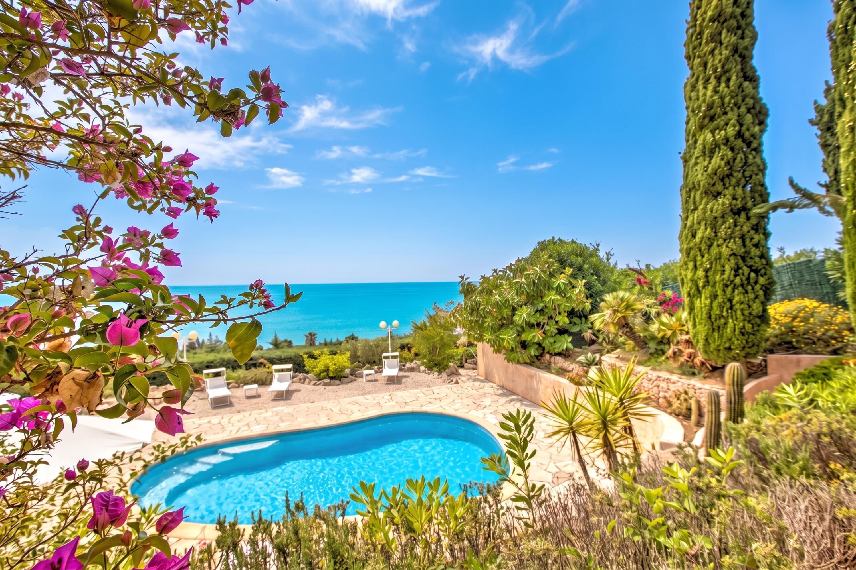 A swimming pool with a view of the sea, surrounded by greenery and cacti.