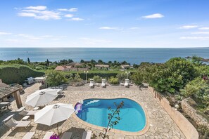 A pool with a stone patio, lounge chairs, umbrellas, and a view of the sea. - Casa Del Sole - Sea view & Swimming pool, St Raphael, France (St Raphael)