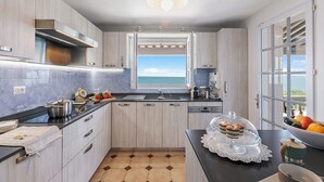 A modern kitchen with a view of the sea, featuring light wood cabinets, a black countertop, and a large window. - Casa Del Sole - Sea view & Swimming pool, St Raphael, France (St Raphael)