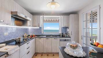 Een moderne keuken met uitzicht op zee, met lichte houten kastjes, een zwart aanrecht en een groot raam.