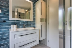 A bathroom with a white vanity, a mirror, and a blue-tiled wall.