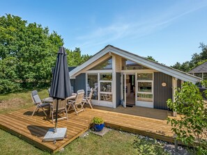 A modern house with a wooden deck, outdoor seating, and a large window.