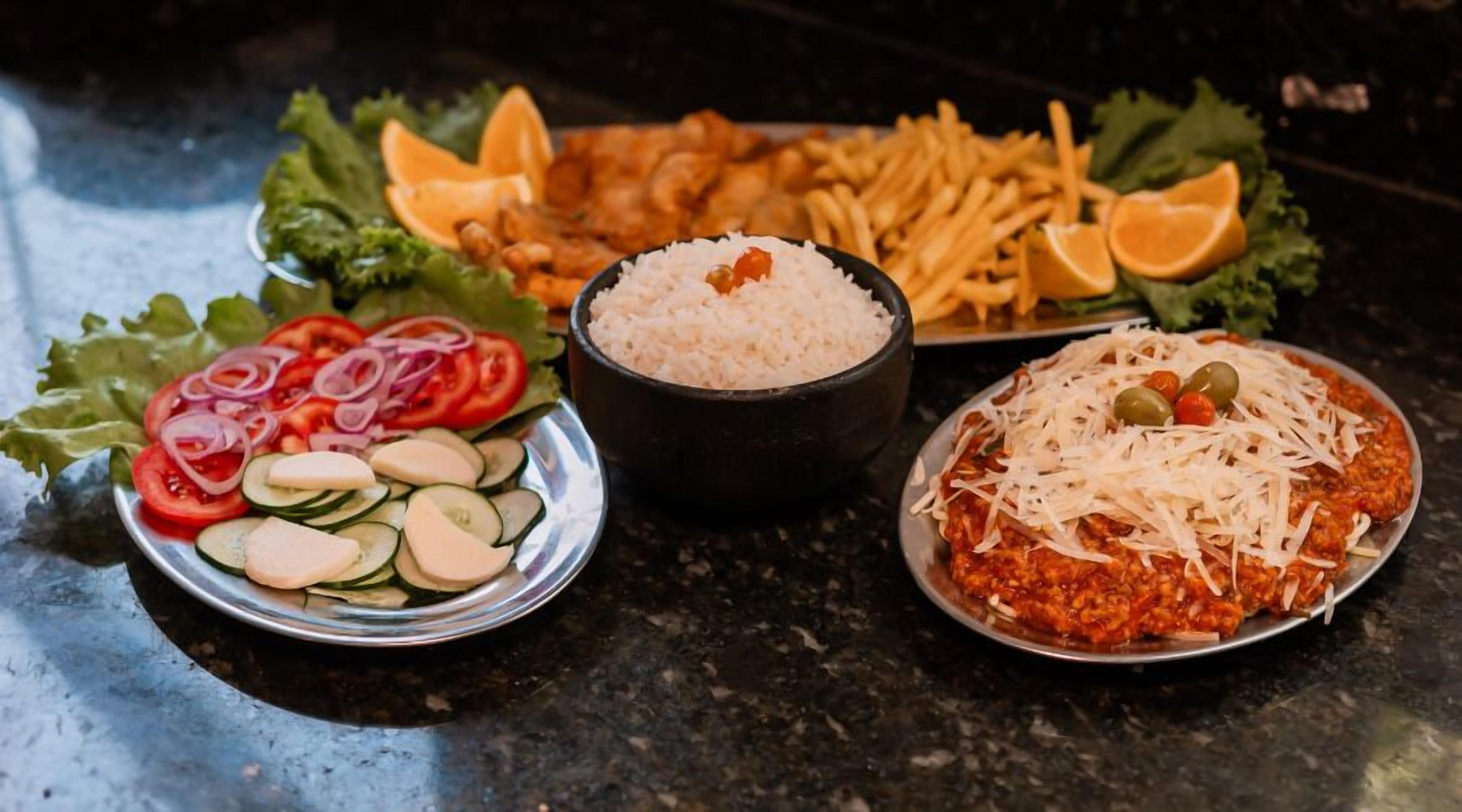A variety of dishes including a salad, rice, fries, and a pasta dish with cheese and olives.