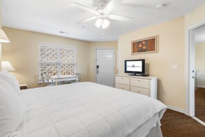 A hotel room with a large bed, a desk with a chair, a television, and a ceiling fan.
