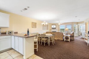 A spacious living area with a dining table, sofas, and a kitchen area with white cabinetry.