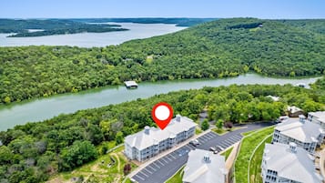 A hotel with a parking lot, surrounded by lush greenery and a lake.