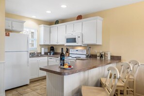 A kitchen with white cabinets, a microwave, a stove, and a dining area with chairs.