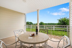 A covered patio with a round table, chairs, a bottle, and a plate with food.