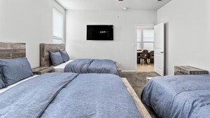 Ett sovrum med två sängar, en tv och en matplats som syns genom en öppen dörr.