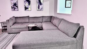 Ein modernes Wohnzimmer mit einem grauen Ecksofa, einem runden Couchtisch und abstrakter Wandkunst.
