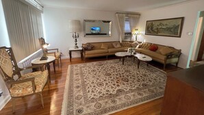 A living room with a sofa, two side tables, a patterned rug, a television, and a painting on the wall.