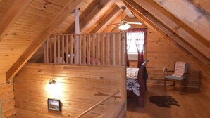Un interno in legno con un soffitto spiovente, una scala, un letto, una sedia e un cane.