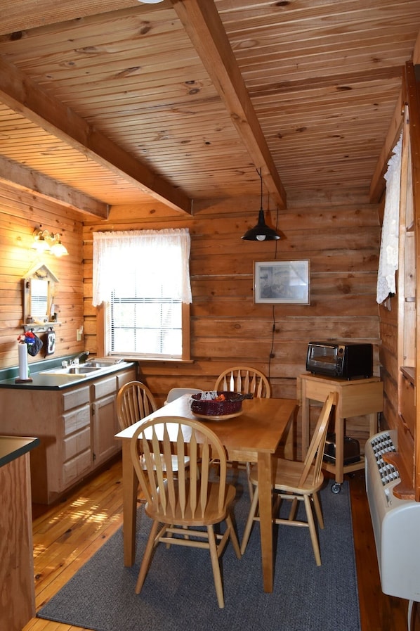 A wooden cabin interior with a dining table, chairs, a kitchen area, and a microwave.