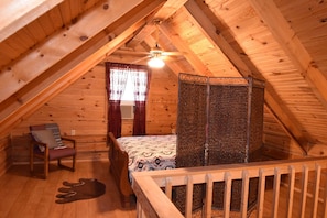 A cozy attic bedroom with a wooden ceiling, a bed, a chair, and a small rug.