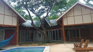 A pool area with a hammock, wooden chairs, and a tree in the center. - Bambu C Casa: Jungle stay, walking distance to Playa Marsella beach. (San Juan del Sur)