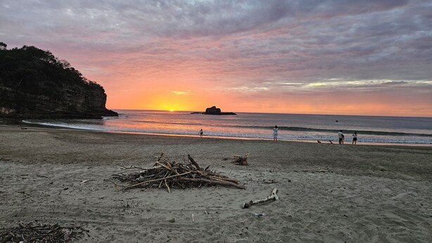 A beach with a sunset, rocky cliffs, and scattered debris. - Bambu C Casa: Jungle stay, walking distance to Playa Marsella beach. (San Juan del Sur)