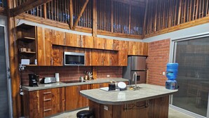 A kitchen with wooden cabinets, a microwave, a refrigerator, a sink, and a water dispenser. - Bambu C Casa: Jungle stay, walking distance to Playa Marsella beach. (San Juan del Sur)
