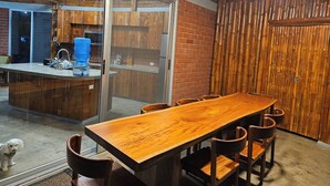 A modern kitchen with wooden cabinets, a large island with a sink, and a dining area with a wooden table and chairs. - Bambu C Casa: Jungle stay, walking distance to Playa Marsella beach. (San Juan del Sur)